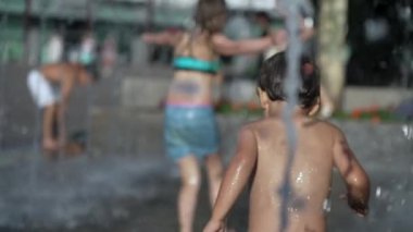 Heyecanlı çocuklar şehirde yaz günü çeşmedeki su jetlerinde oynuyorlar. Çocuk ağır çekimde eğleniyor.