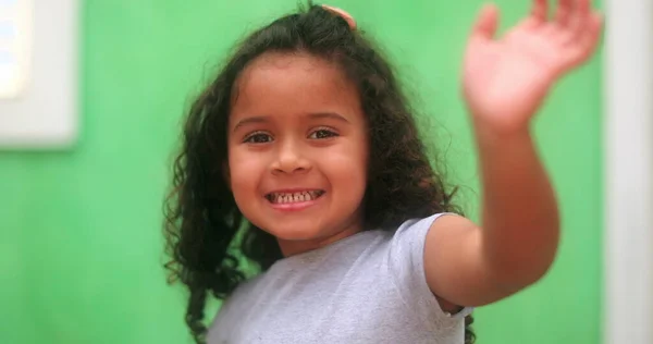 Hispanic little girl waving hello to camera. South american kid waves hi