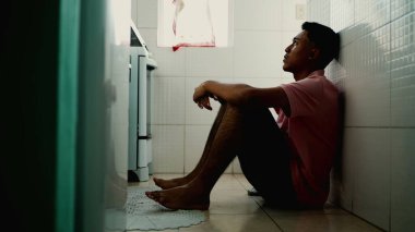 Endişeli genç bir Güney Amerikalı yerde oturmuş endişeli duygular hissediyor. Stresli insan modern sorunlarla boğuşuyor. Yalnız Brezilyalı adam.