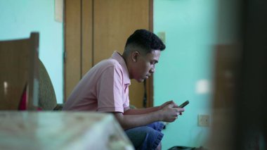 İspanyol bir adam kanepede oturuyor ve telefon kullanıyor. Akıllı telefon tutan bir Latin.