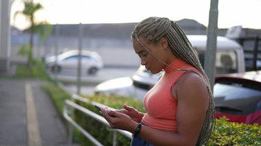 Açık havada tablet kullanan genç bir zenci kadın. Dışarda internette saç stili tarayan İspanyol asıllı bir Brezilyalı.