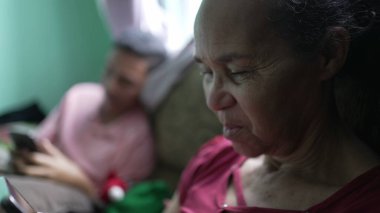 Evde telefon kullanan son sınıf öğrencisi bir kadın. Kanepede oturan zeki telefon cihazını tutan samimi, İspanyol bir yaşlı.