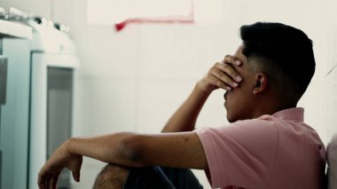 Depressed man sitting on floor. Sad unhappy person holding his forehead suffering from mental illness
