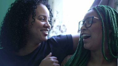 Samimi kız kardeşler evlerinde sohbet ediyorlar. İki genç İspanyol kadın konuşuyor ve gülüyor.