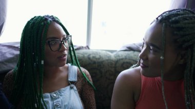 İki Latin kökenli genç Latin kadın evde saç örgüleriyle konuşuyorlar.