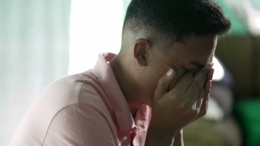 Çaresiz genç adam umutsuzluk ve umutsuzluk hissediyor. İspanyol bir Güney Amerikalı, elleriyle yüzünü kapatarak ağlıyor.