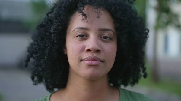 真剣な表情で屋外に立っているカメラのクローズアップ顔の肖像画を見ている1人の若い黒人女性 巻き毛のある自然なカジュアルな美しさ — ストック写真