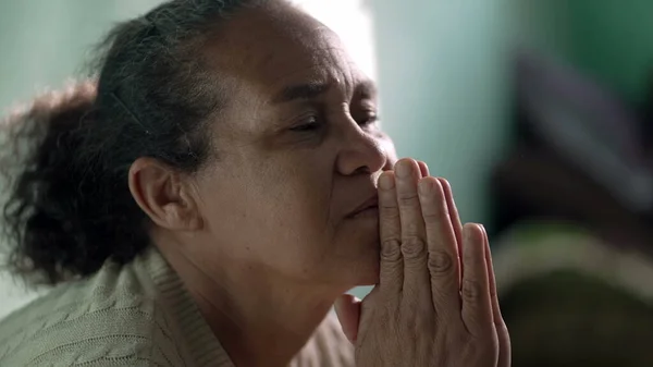 Older woman praying to God at home. One hispanic senior lady in prayer closeup face. Hispanic South American person