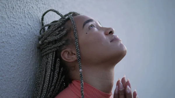 One spiritual young black woman praying to God pleading help and support. A faithful Brazilian adult girl in prayer looking up at sky with HOPE and FAITH