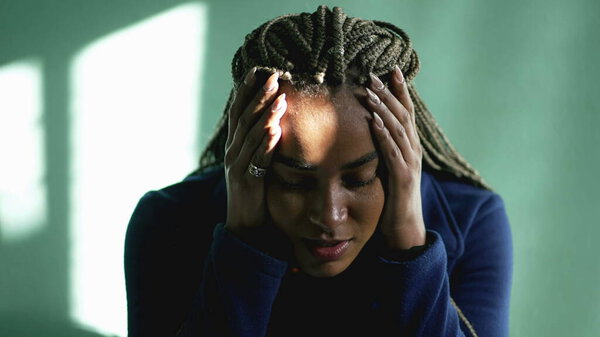Desperate young woman in crisis at home. African American woman suffering from mental illness in despair. One South American black person in desperation