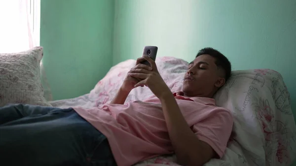 Uppriktig Sydamerikansk Ung Man Ligger Sängen Med Hjälp Smartphone Enhet — Stockfoto