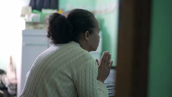 One senior woman praying at home by bedside. A spiritual older black lady prays having HOPE