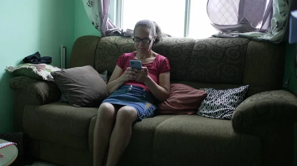 Jedna Szczera Latynoska Seniorka Używająca Telefonu Siedząca Kanapie Domu Przypadkowa — Zdjęcie stockowe