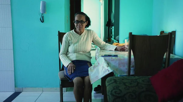 A thoughtful senior black woman sitting at apartment. A pensive hispanic latin south american senior person