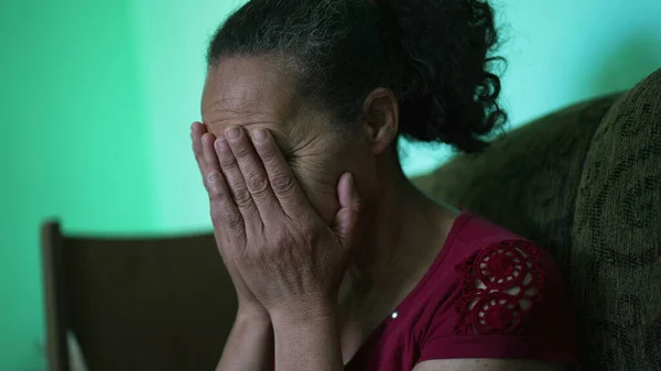 One depressed senior woman covering face with regret. An older hispanic south american older lady feeling anxiety