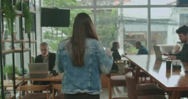 Tezgahtan kahveyi alan ve arkadaşlarıyla masaya oturan mutlu genç bir kadın. Kadın müşteri kahve dükkanının içinden espresso siparişini alıyor.