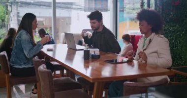 Bir grup arkadaş kahve masasında oturmuş espresso yudumluyorlar. Restorandaki küçük iş yerindeki mutlu erkek ve kadın müşteriler.