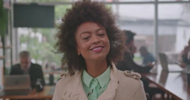 Kafenin içinde kameraya bakan Afro-Amerikalı genç bir kadının portresi. Mutlu, zarif, kıvırcık saçlı yetişkin bir kız.