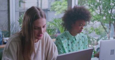 Laptop bilgisayarlarının önündeki kafede iki farklı genç kadın. Uzaktan çalışan kadın iş arkadaşları