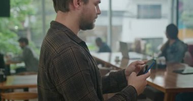 Kahve dükkanında cep telefonu kullanan genç bir adam. Müşteri interneti taramak için akıllı telefon kullanıyor