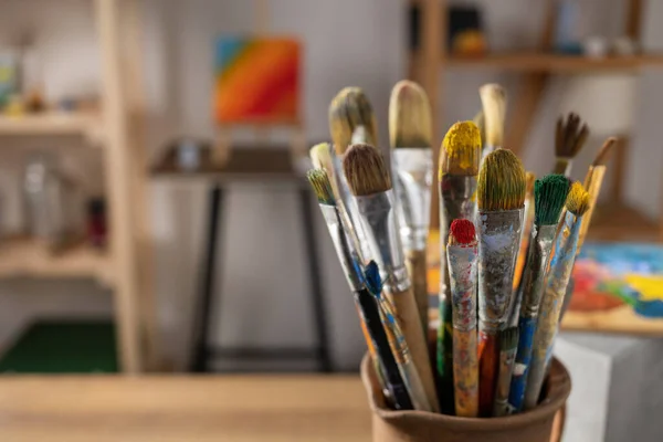 Sanatçı malzemeleri ahşap masada. Çamur sürahisinde boya fırçası ve ahşap masa arkaplan dokusunda resim boyama aletleri. Ressam stüdyosunda resim yapmak için boya fırçası