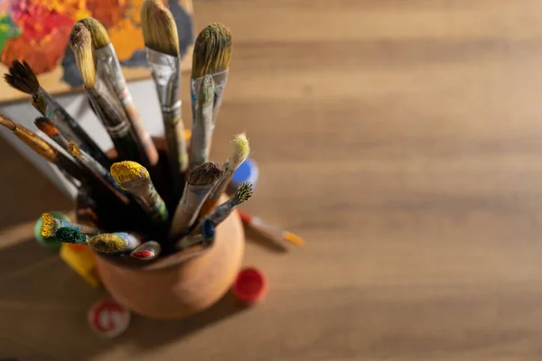 Sanatçı malzemeleri ahşap masada. Çamur sürahisinde boya fırçası ve ahşap masa arkaplan dokusunda resim boyama aletleri. Ressam stüdyosunda resim yapmak için boya fırçası