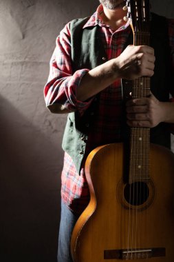 Akustik gitar tutan adam. Duvara yakın klasik akustik gitarıyla stüdyoda müzisyen.