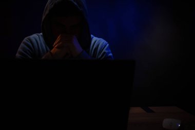 Bilgisayar laptopunun önünde bir hacker var. Karanlık oda arka planında bir hacker.