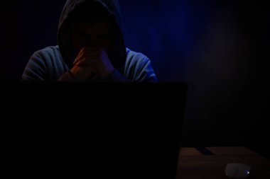 Bilgisayar laptopunun önünde bir hacker var. Karanlık oda arka planında bir hacker.