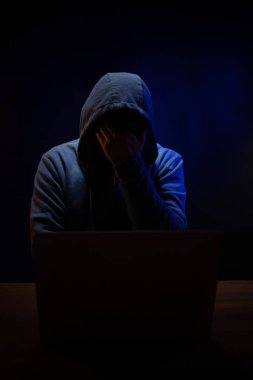 Bilgisayar laptopunun önünde bir hacker var. Karanlık oda arka planında bir hacker.