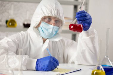 Bilim adamı araştırma sonuçlarını yazıyor ve sıvı reaksiyonla tüp test ediyor. Laboratuvar bilimcisi ve kimya laboratuarı cam eşyalar.