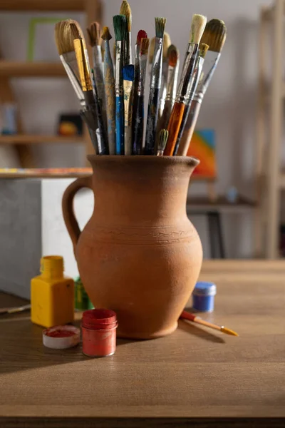 Sanatçı malzemeleri ahşap masada. Çamur sürahisinde boya fırçası ve ahşap masa arkaplan dokusunda resim boyama aletleri. Ressam stüdyosunda resim yapmak için boya fırçası
