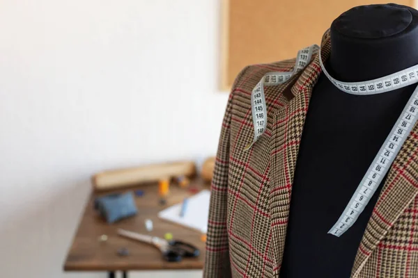 Suit jacket on tailor mannequin and sewing tools. Concept of clothes atelier workplace