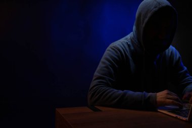 Hacker dizüstü bilgisayarda çalışıyor. Karanlık oda arka planında Hacker saldırısı