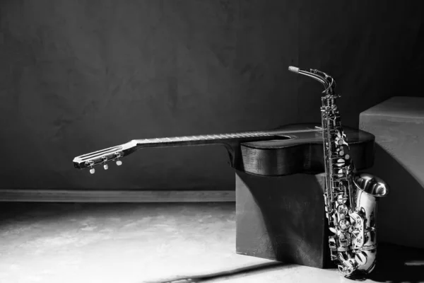 Eski akustik gitar ve yerde saksafon. Stüdyoda müzik konsepti ve duvarın yanında müzik aleti