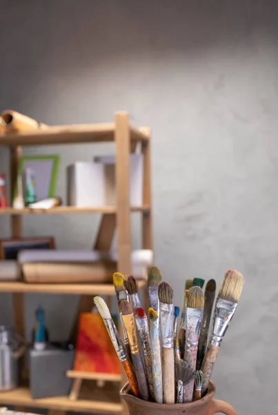 Sanatçı malzemeleri ahşap masada. Çamur sürahisinde boya fırçası ve ahşap masa arkaplan dokusunda resim boyama aletleri. Ressam stüdyosunda resim yapmak için boya fırçası