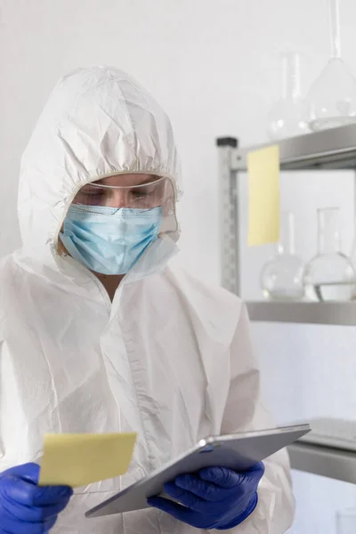 Bilgisayar tableti üzerinde çalışan bilim adamı sıvı reaksiyonla test tüpüne bakıyor. Laboratuvar bilimcisi ve kimya laboratuarı cam eşyalar.