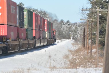 Kışın çam ağaçlarıyla karlı yollarda giden tren.