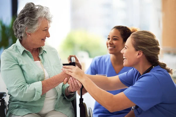 Постріл усміхненої жінки-лікарки і медсестри розмовляють з старшою жінкою в інвалідному візку — стокове фото