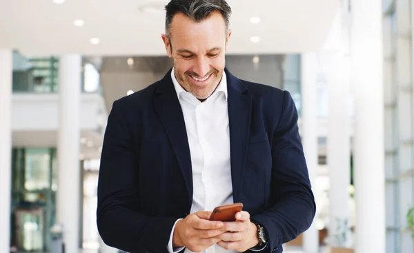 Instant connection brings instant good news. Shot of a mature businessman using a smartphone while walking through a modern office. — Fotografia de Stock
