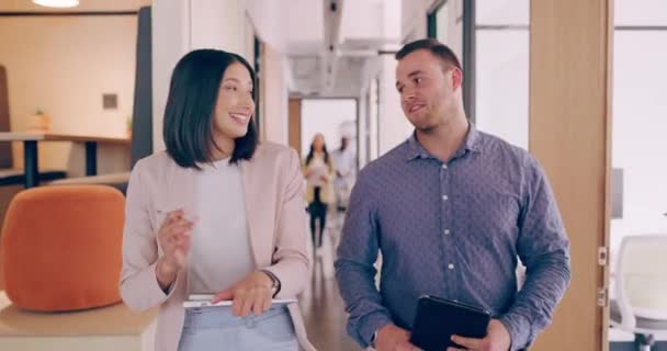 4k video footage of two young business colleagues chatting as they walk though the office — Stockvideo