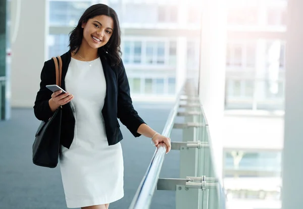 Every day is smiling day if you love your job. Cropped portrait of an attractive young businesswoman smiling while holding a smartphone in a modern office. — Stockfoto