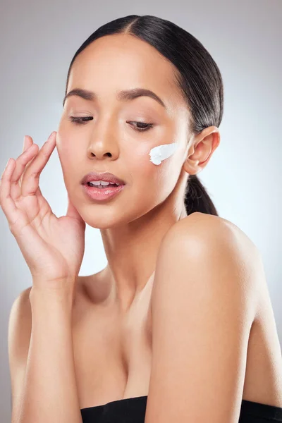 Siempre termino con SPF. Foto de estudio de una hermosa joven aplicando crema hidratante en su cara sobre un fondo gris. — Foto de Stock
