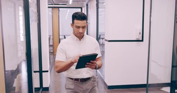 4k video footage of a young businessman working on a tablet and checking the time on his wrist watch as he walks through his office — Video
