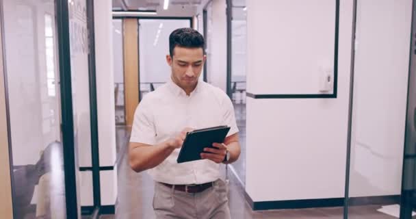 4k video footage of a young businessman working on a tablet and checking the time on his wrist watch as he walks through his office — стоковое видео