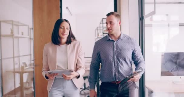 4k video footage of two young business colleagues chatting as they walk though the office — Vídeos de Stock