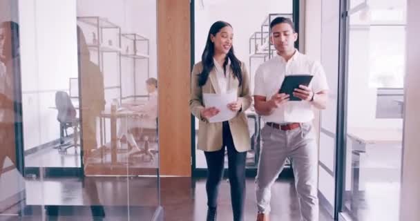 4k video footage of a young businessman going through notes on his tablet with a female colleague while they walk through the office — Vídeo de Stock