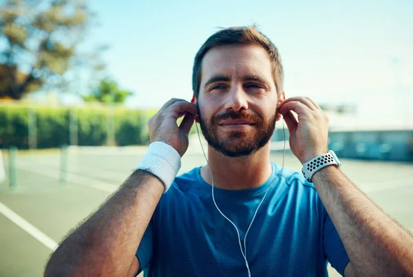 A preparar música para combinar com o seu humor. Tiro de um jovem desportivo ouvindo música enquanto se exercita em uma quadra de tênis. — Fotografia de Stock
