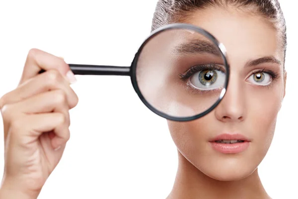 Magnifying her best features. Studio shot of a beautiful woman with a magnifying glass in front of her eye. — Stock Photo, Image