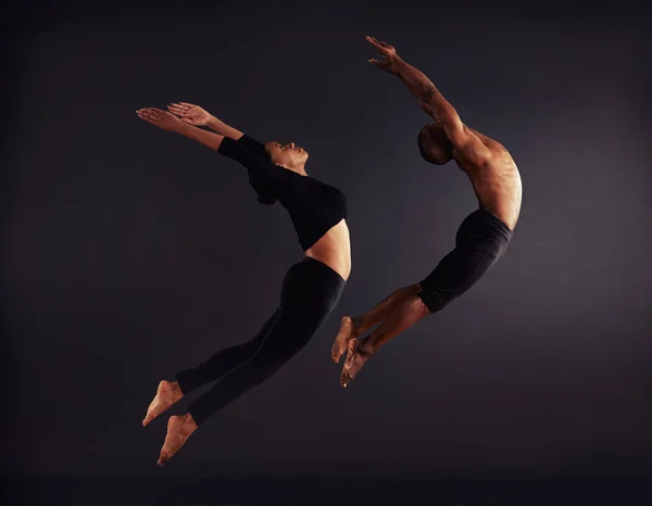 Liberdade de voo. Uma dançarina contemporânea feminina e masculina realizando uma pose dramática na frente de um fundo escuro. — Fotografia de Stock